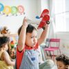 Asian toddler wearing a red shirt and overalls holding a red biplane toy above his head making a determined face